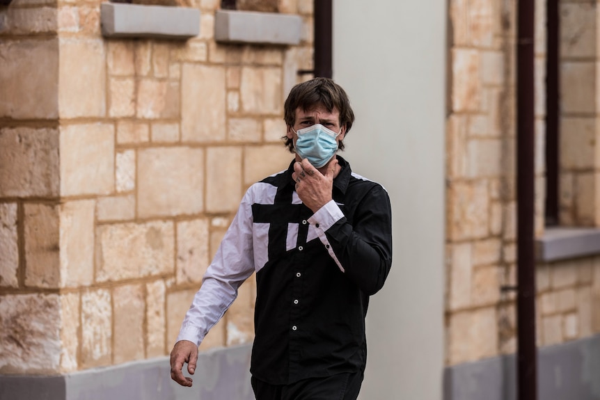 A man wearing a mask leaves a court building.  