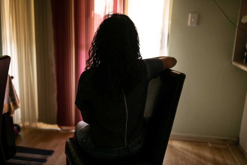 A girl sits on a chair in the dark