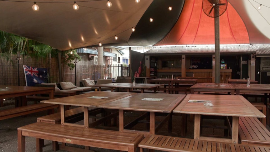 A covered outdoor dining area, filled with wooden tables and benches, empty of people.