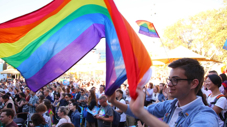 A man holds a rainbow flag among a crowd at a Yes rally in Perth