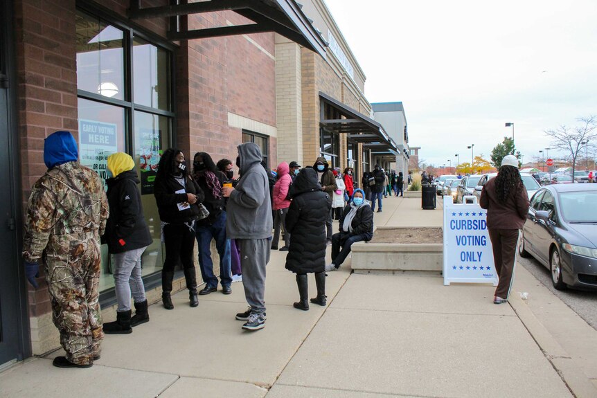 A long line of people standing outside a building near a sign reading "curbside voting only"