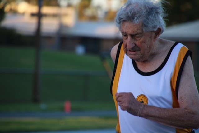 An elderly man runs in a running singlet in the early morning light.