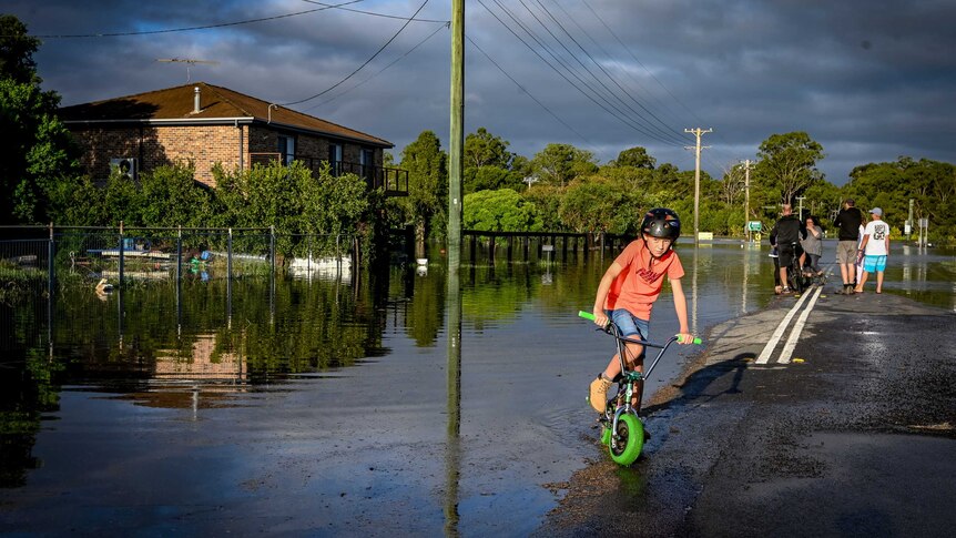 A child on a bike with flood water on the side.