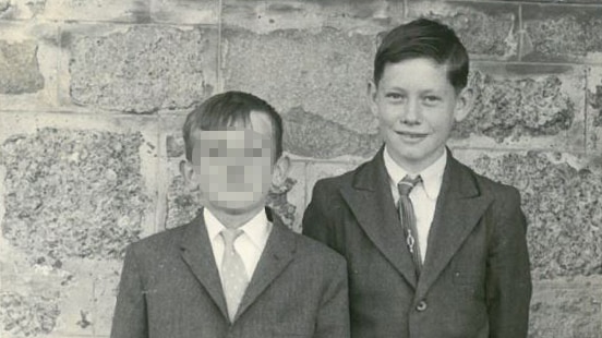 Two boys stand against a stone wall in a black and white picture.