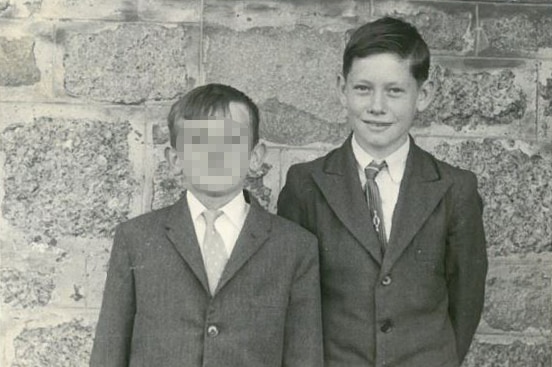 Two boys stand against a stone wall in a black and white picture.