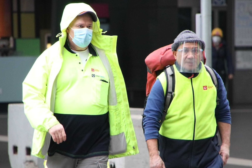 Two workers wearing fluro, one with a mask, the other with a face shield