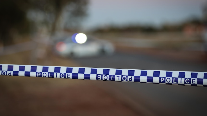 Police tape with a police car blurred in the background