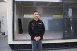 A man stands in front of a prefabricated home in a warehouse.
