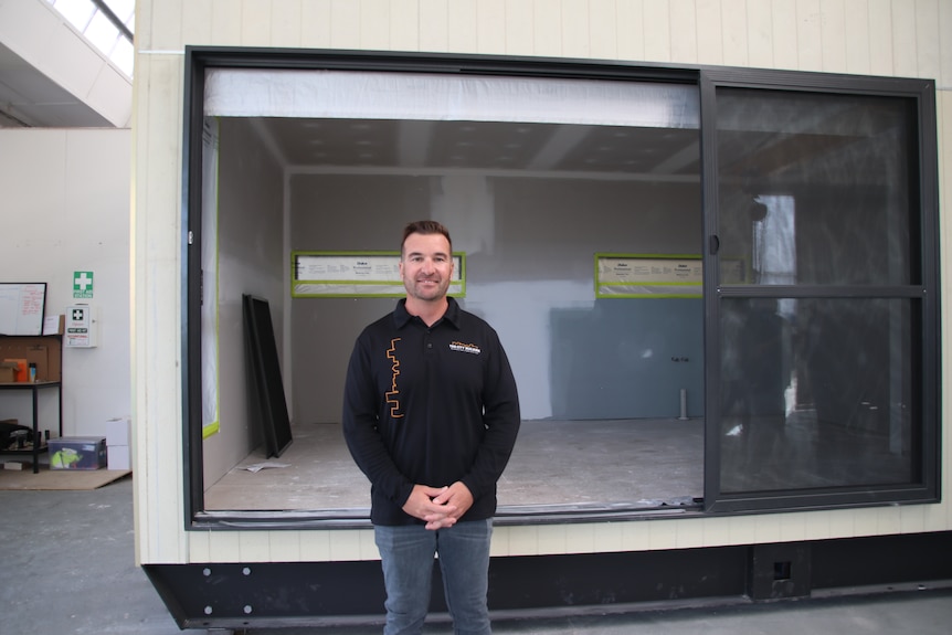 A man stands in front of a prefabricated home in a warehouse.