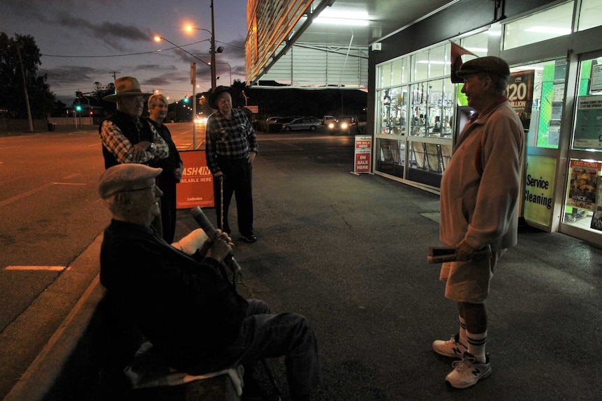 A group of older people chat outside a newsagent early in the morning
