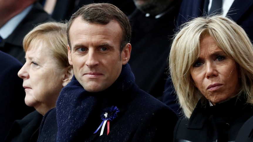 Angela Merkel, Emmanuel Marcon and Brigitte Macron wearing black clothing. Mr Macron has a remembrance ribbon pinned on his coat