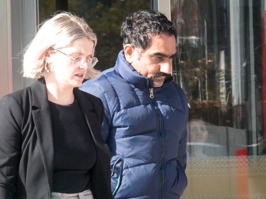 A man in a puffer jacket walks alongside a building with a female lawyer.