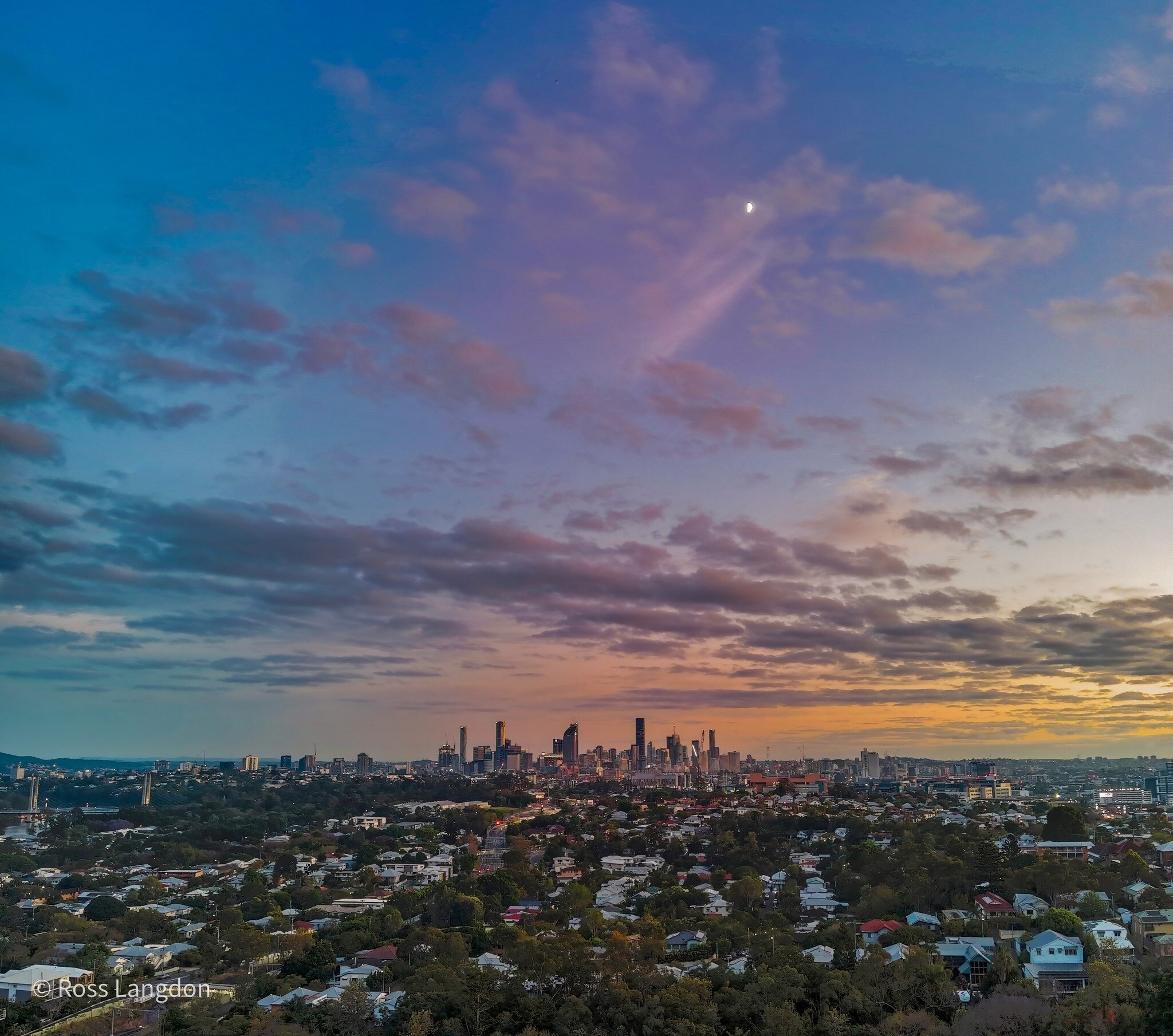 a far away view of brsibane city with high rises in the skyline under a setting sun