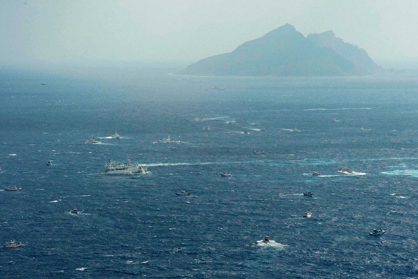 Ships in turquoise waters leave white streaks as twin mountain ranges peak in the distance amid fog.