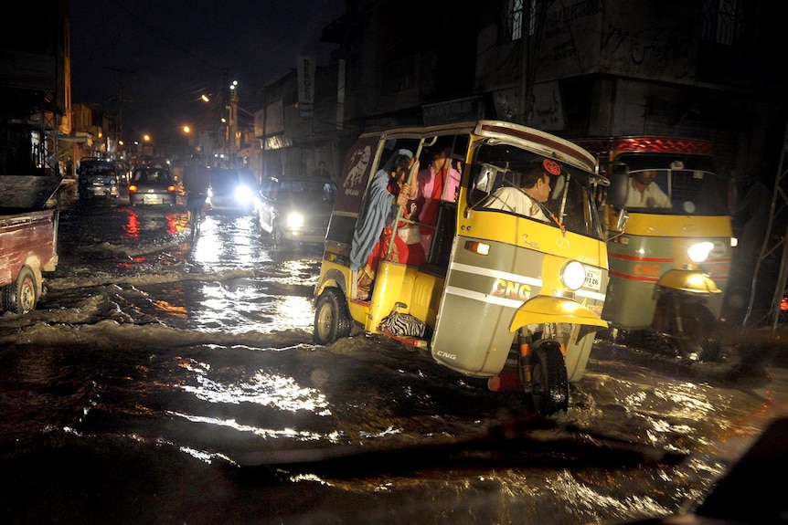 Pakistani commuters cross a flooded street in an auto-rickshaw following heavy monsoon rain