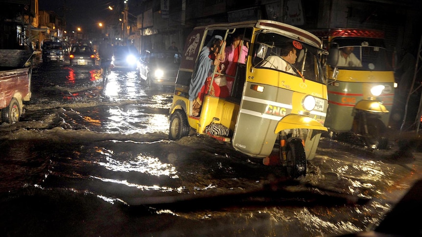 Pakistani commuters cross a flooded street in an auto-rickshaw following heavy monsoon rain