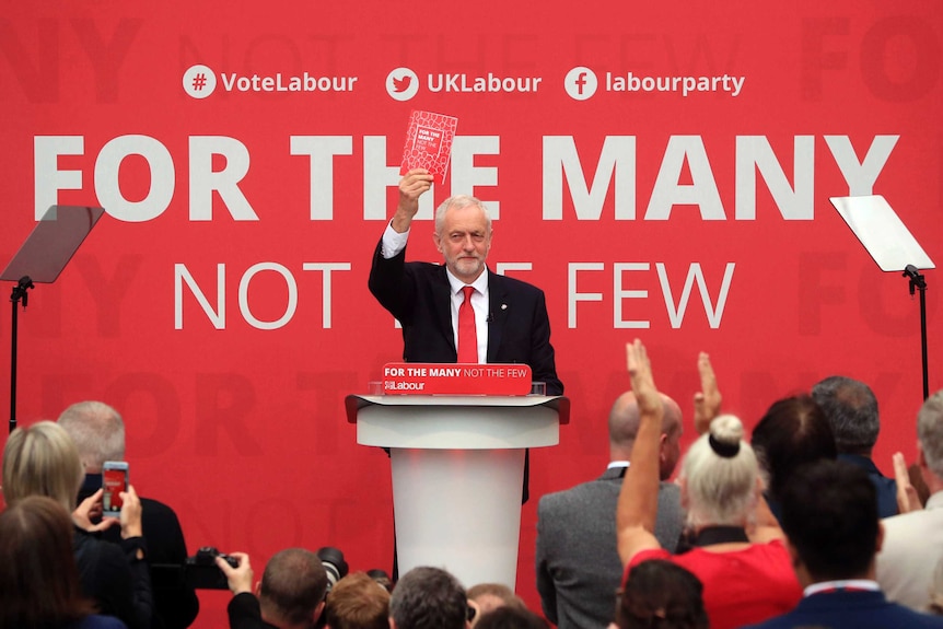 Jeremy Corbyn stands at a lectern holding up Labour's election manifesto.