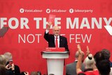 Jeremy Corbyn stands at a lectern holding up Labour's election manifesto.