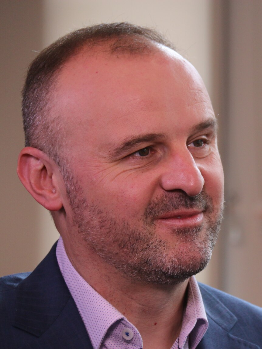 A man in a suit sits in a business chair, mid-conversation