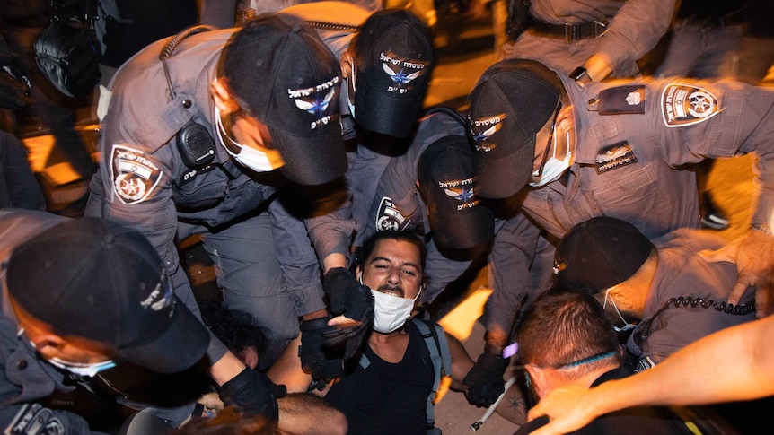 A man is held down on the ground by at least six police officers