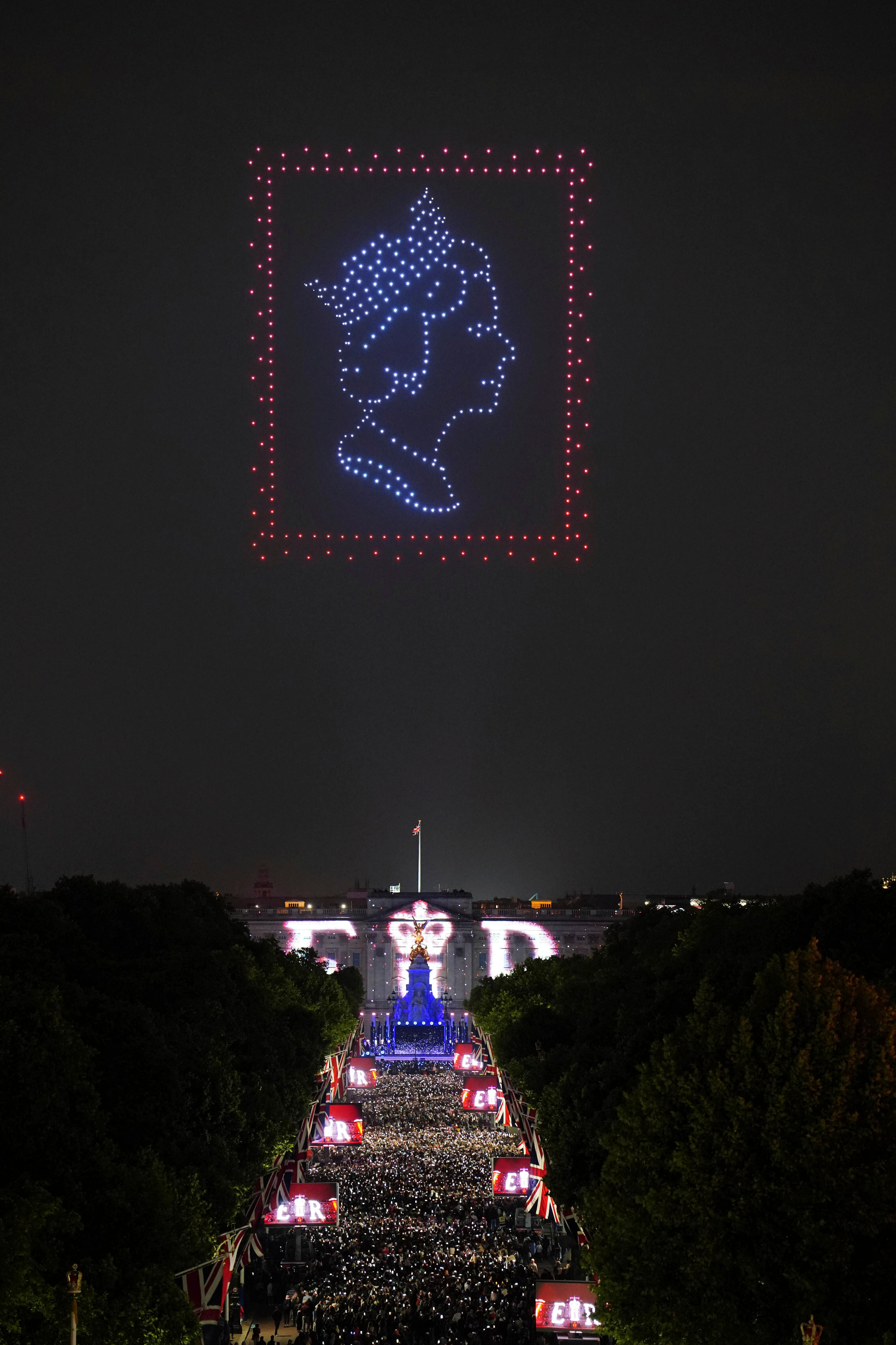 Drone cu lumini care prezintă forma unei regine pe un timbru poștal deasupra Palatului Buckingham