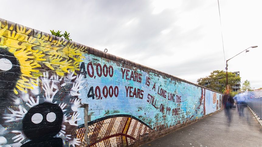 Colour photograph of 40,000 Years mural on Lawson Street bridge in the suburb of Redfern on a cloudy day.