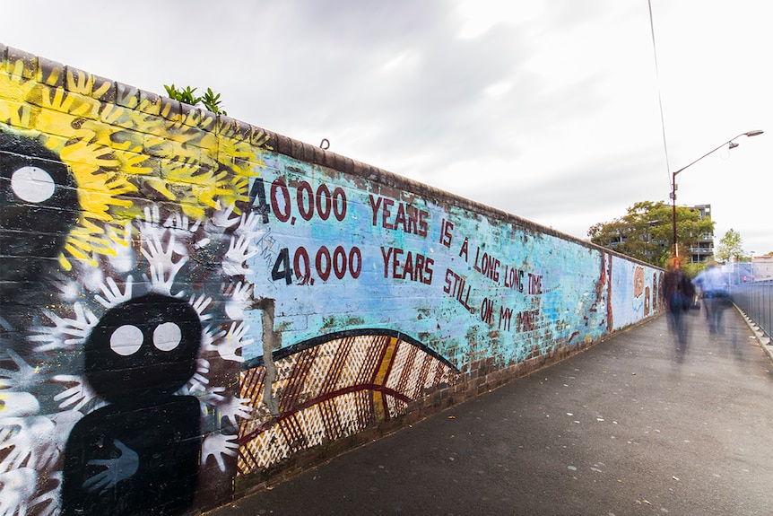Colour photograph of 40,000 Years mural on Lawson Street bridge in the suburb of Redfern on a cloudy day.