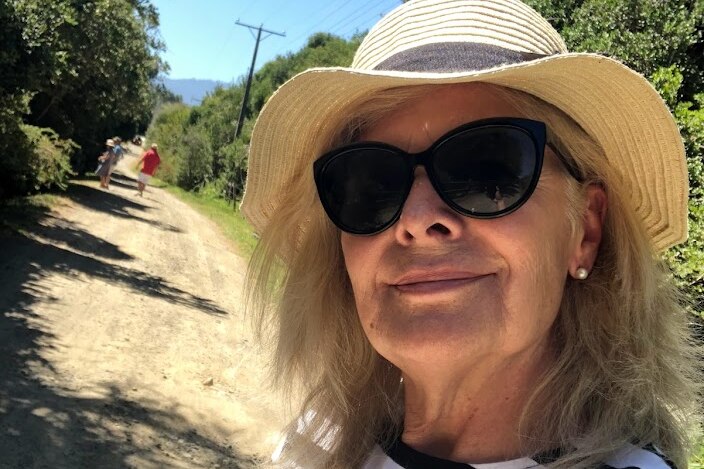 An older woman takes a selfie in the countryside.