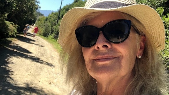 An older woman takes a selfie in the countryside.