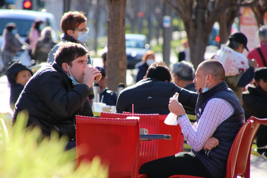 Two men eat and drink outside at a cafe.