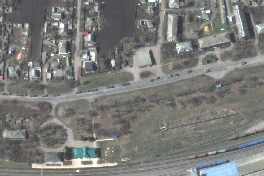 A satellite image shows part of a convoy of several hundered armoured vehicles and trucks passing along a main road past a town.