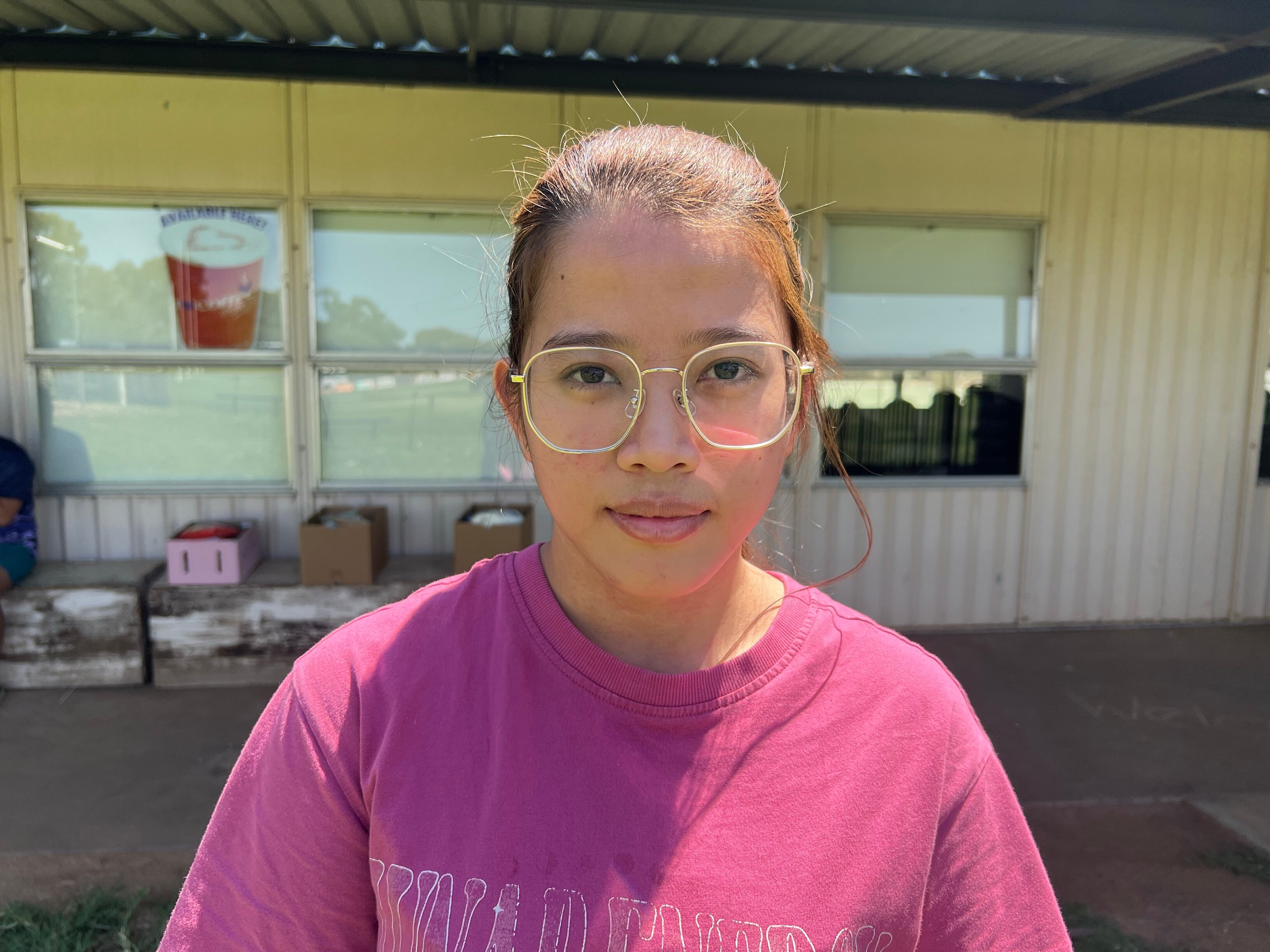 Young woman with her hair pulled back into a ponytail, wearing glasses, looks into the camera with serious expression.