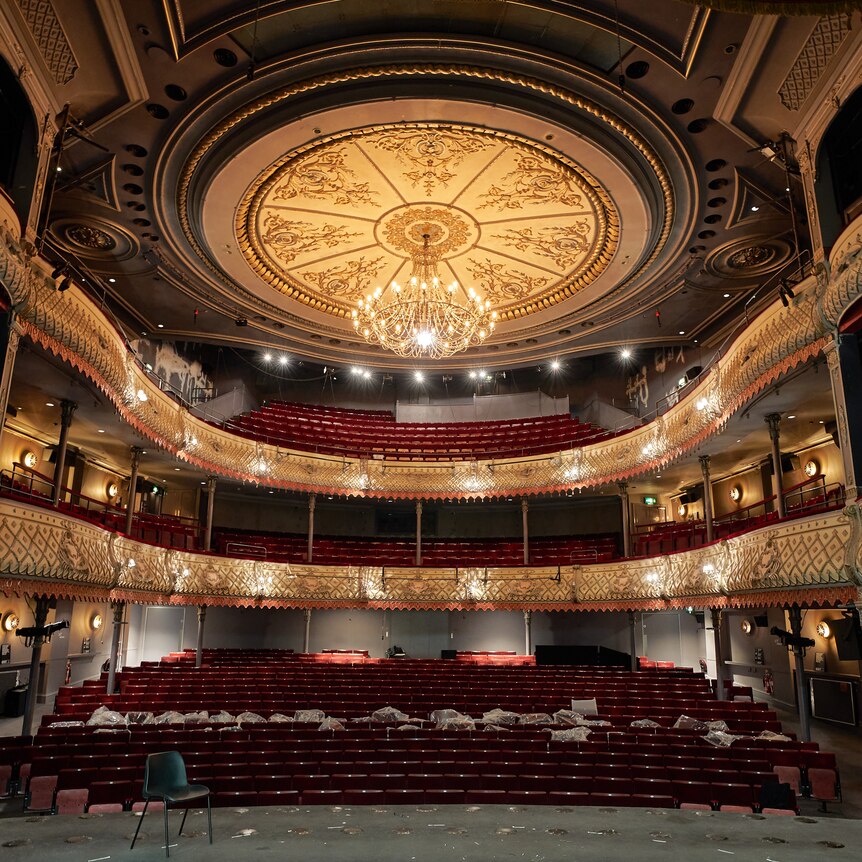 The view from the stage of an ornate theatre with stalls, a dress circle and balcony. A grand chandelier hangs above.