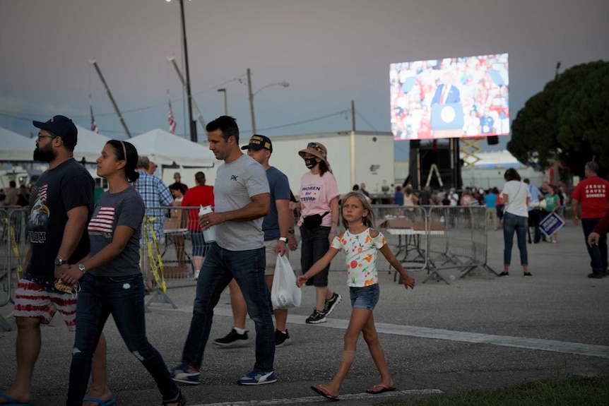 A young girl looks at the camera as she walks through a rally crowd