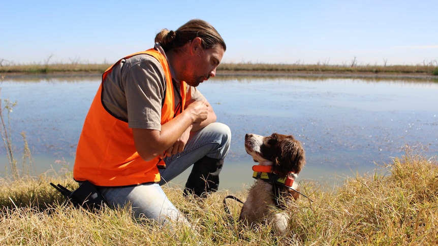 Ryan Tate and conservation detection dog Connor sit by the edge of Barren Box Swamp near Griffith in NSW.