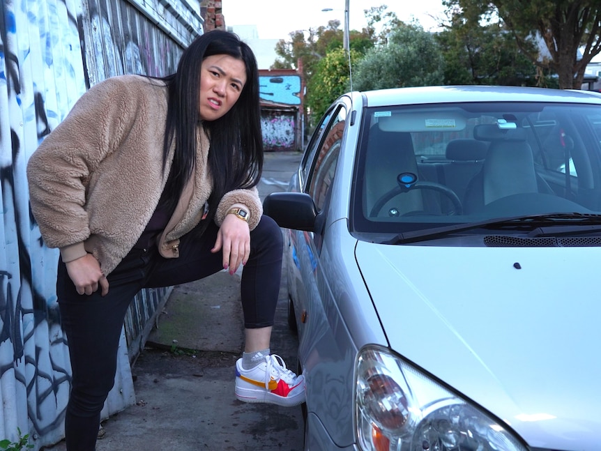 Annie Louey stands next to her old, silver car with her left foot propped up on a front tyre