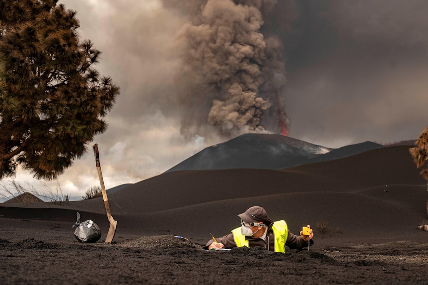 A scientist stands in a hole with a yellow vest while lava spews behind him.