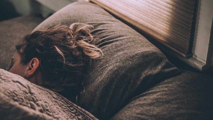 A photo of a woman sleeping, light is coming through the blinds from outside the room.