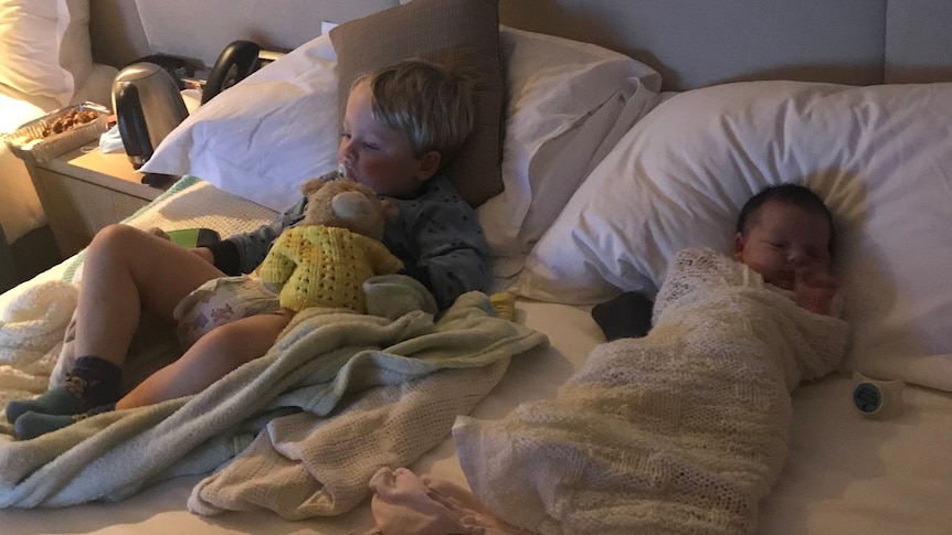 A toddler and newborn baby lay on a hotel bed