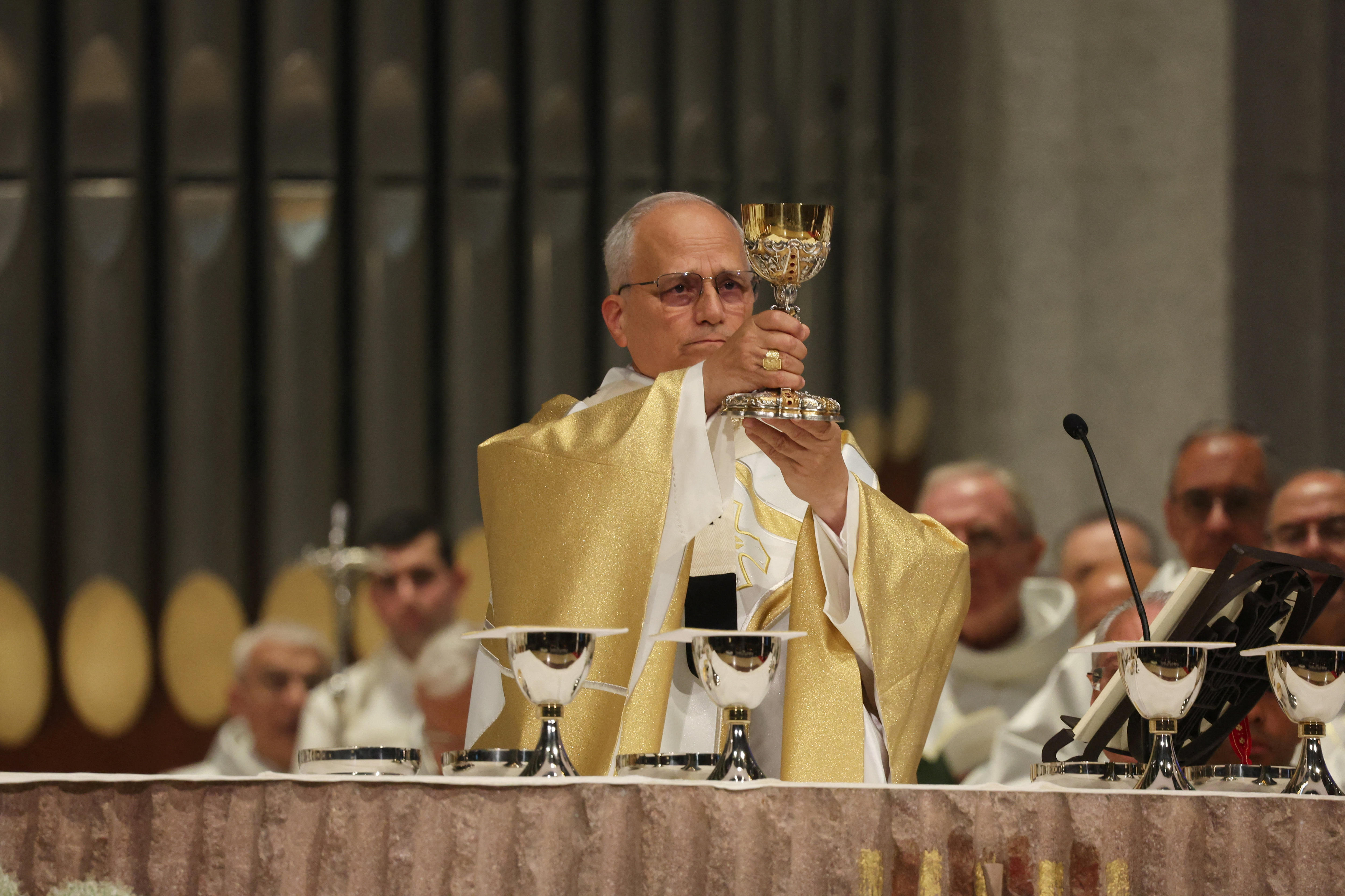 Pope Leo in gold and white robes holding up a golden goblet, over a stone platform with other silver goblets.