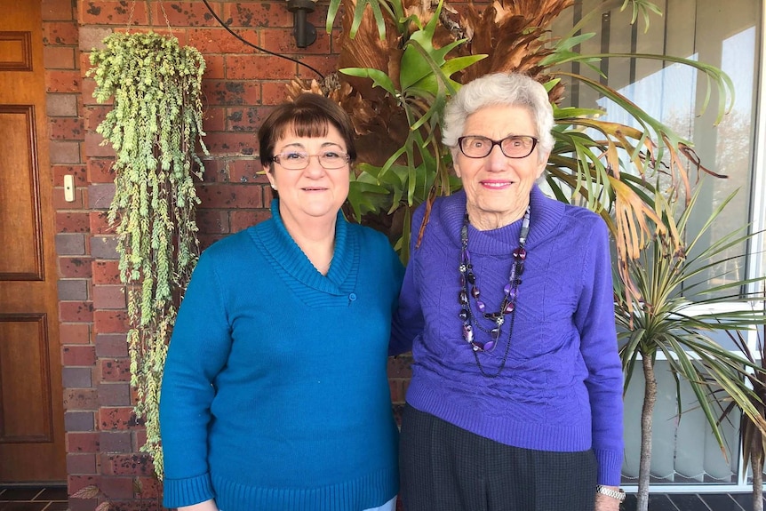 Two middle-aged ladies stand outside a house smiling for the camera