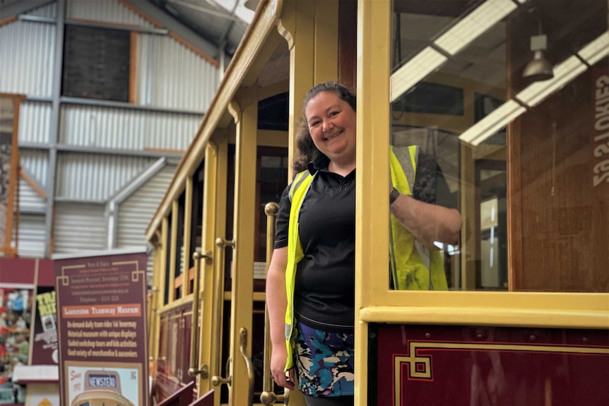 A woman in a hi-vis vest stands on a historic tram.