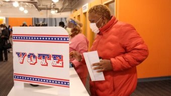 A woman in a face mask stands at a polling booth