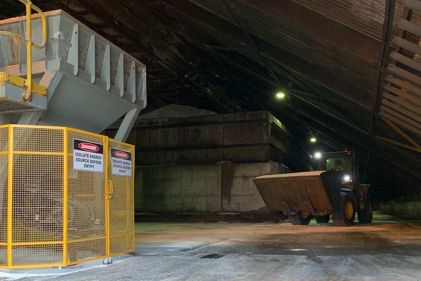 A large loader with a scoop of ammonium nitrate in the front driving through a large shed