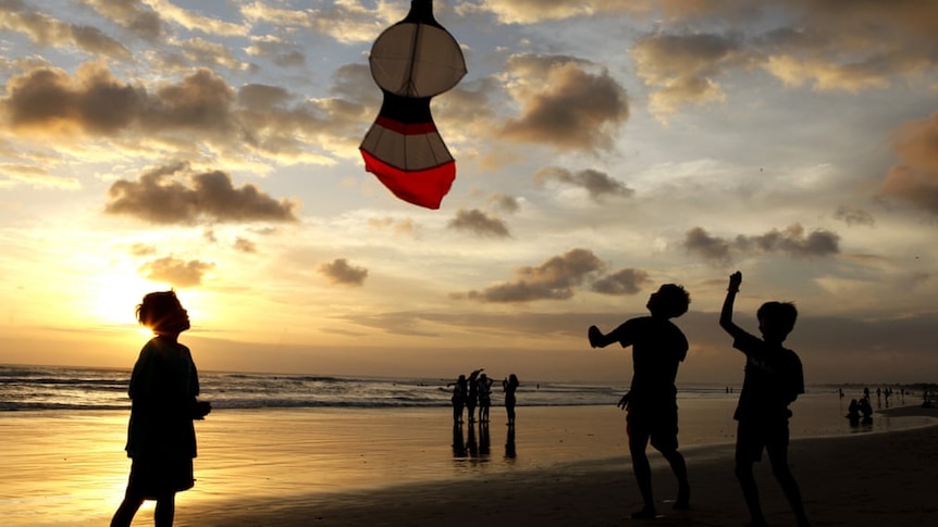 Boys play with a kite on a beach at sunset