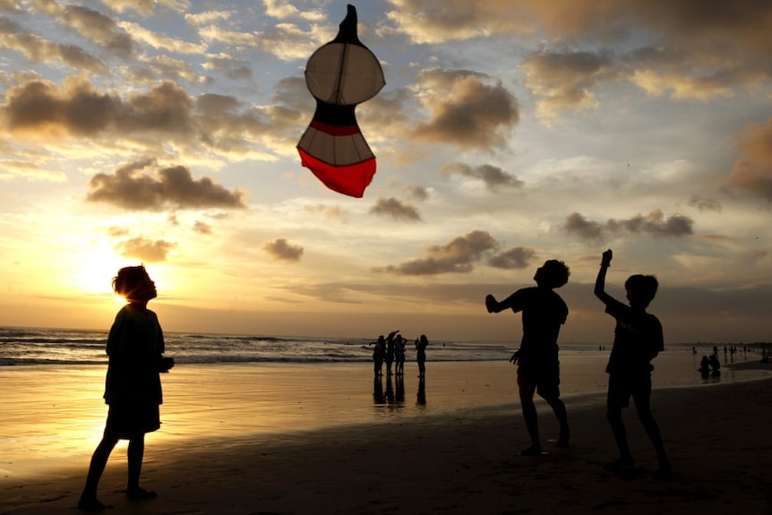 Boys play with a kite on a beach at sunset