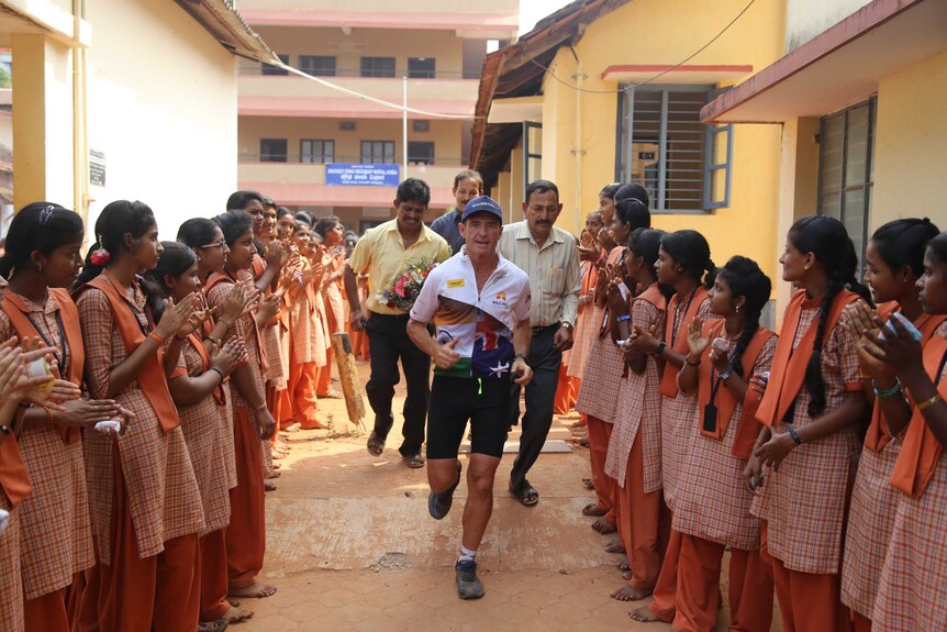 Pat Farmer runs through the grounds of a school through a group of school girls cheering him on.