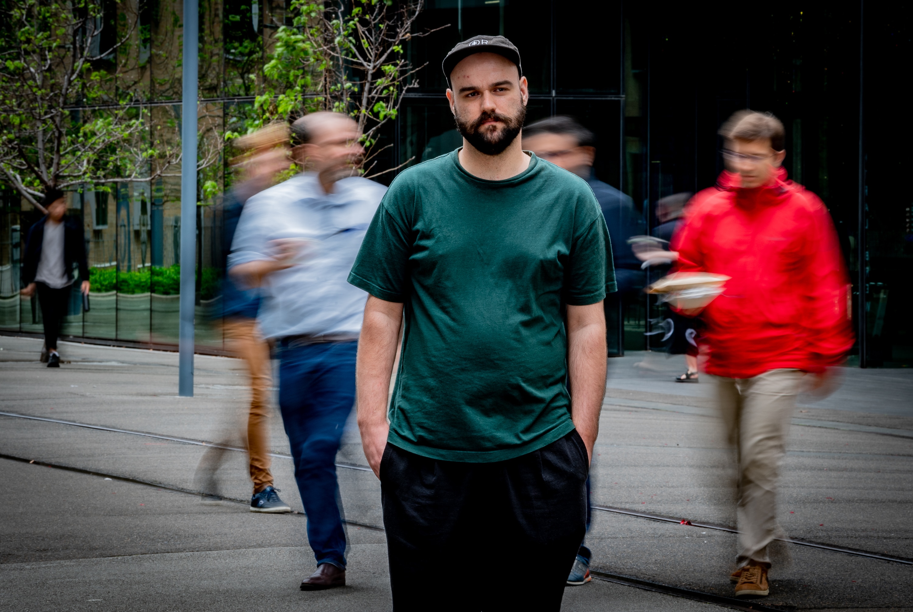 A young man in a green shirt standing in a street while people walk past him