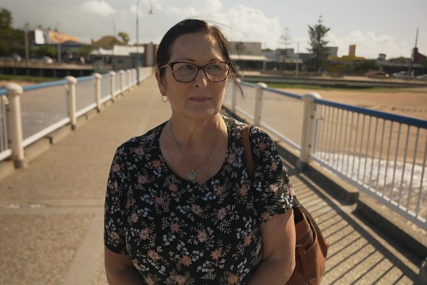 A woman with brown hair and glasses walks along a pier.