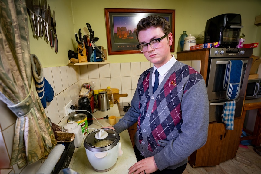 A man wearing glasses and an argyle jumper at a rice cooker in a home kitchen